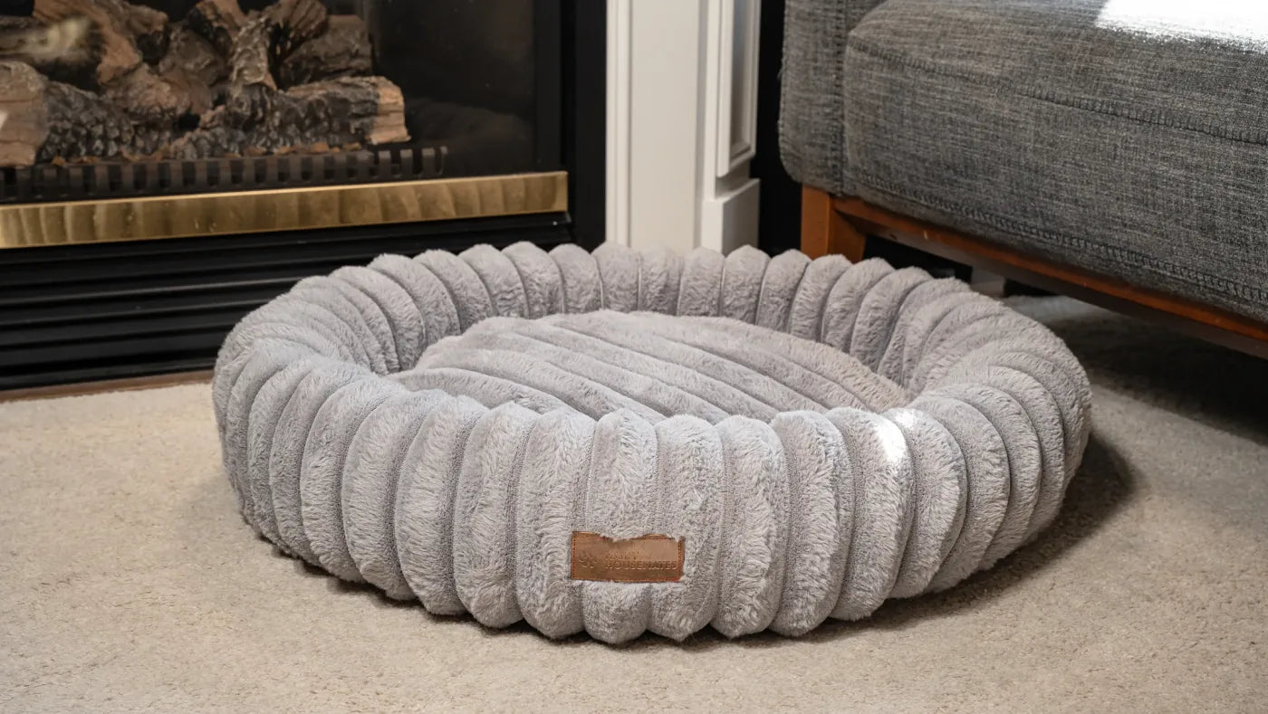 Slate corduroy dog bed, photographed on a cream rug beside a sofa